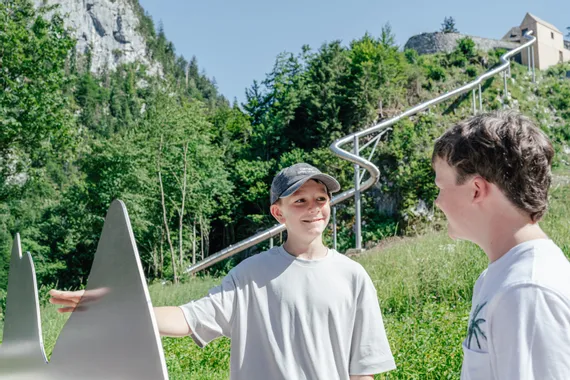 Zwei Jungen unterhalten sich neben einer Metallinstallation vor einer Berg-Rutsche im Freien